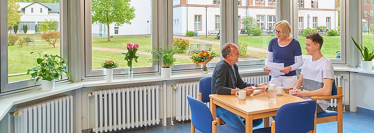 Mehrere Personen sitzen an einem vor Fenstern