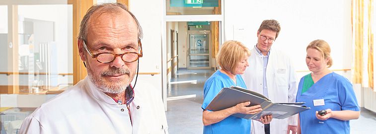 Prof Dr med Matthias Strittmatter schaut in die Kamera und Team im Hintergrund