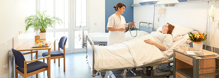 Pflegekraft spricht mit Person in Krankenbett