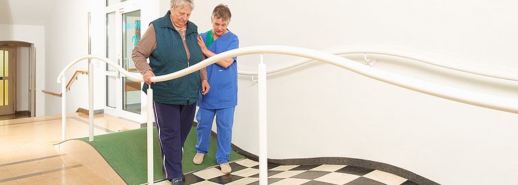 Pflegekraft hilft Frau beim Laufen