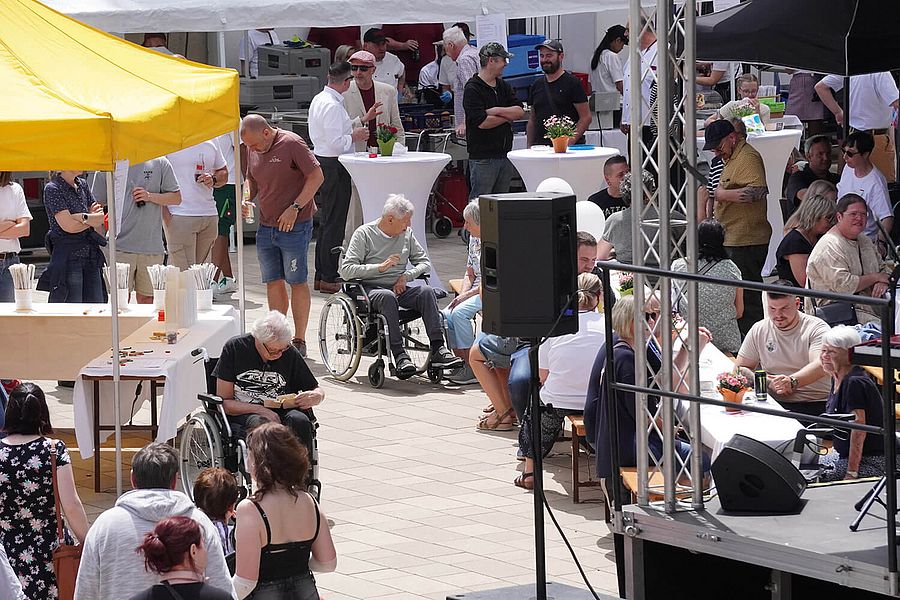 Eine Aufnahme des Tags der offenen Tür aus erhöhter Perspektive. Man sieht Besucher auf der Café-Terrasse, verschiedene Stände und eine Musikbühne.
