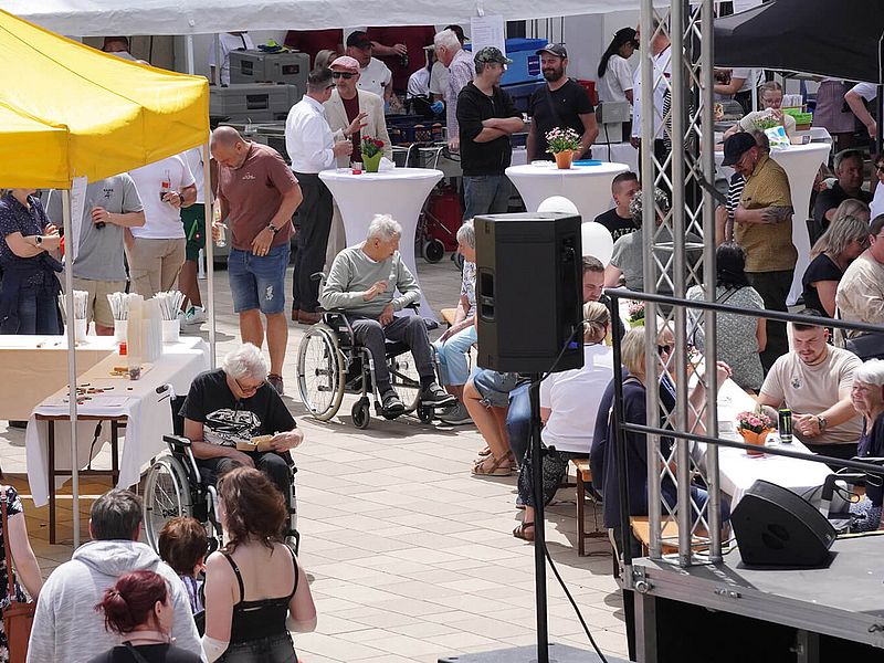 Eine Aufnahme des Tags der offenen Tür aus erhöhter Perspektive. Man sieht Besucher auf der Café-Terrasse, verschiedene Stände und eine Musikbühne.