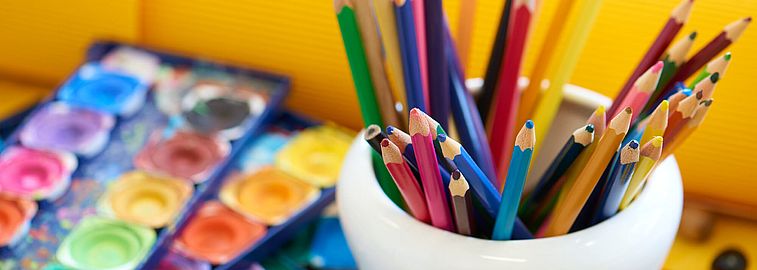 Holzbuntstifte und Farbmalkästen liegen auf einem Tisch